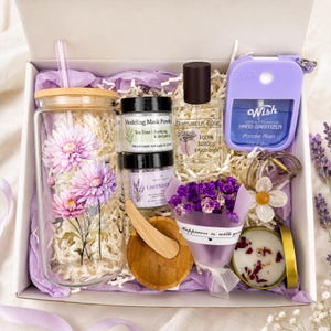 May include: A gift box containing a glass tumbler with pink chrysanthemum decals, a tea tree modeling mask powder, a Damascus rose hydrosol spray, a purple Wish hand sanitizer, a lavender bath soak, a wooden scoop, dried purple flowers, and a candle.