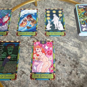 K&ouml;nnte beinhalten: Ein Tarotkartenspiel mit farbenfrohen Illustrationen. Die Karten zeigen Bilder von Stab-Ass, Ritter der St&auml;be, Sechs der Pentakel, Neun der Schwerter und Die Kaiserin. Ein Kartenspiel mit Scooby Doo-Design ist ebenfalls vorhanden.