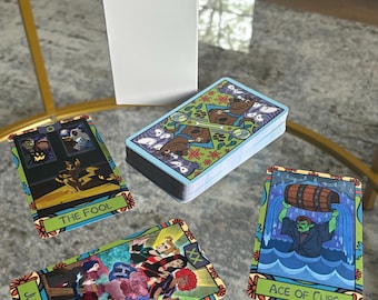 May include: A deck of tarot cards with colorful illustrations, including "The Fool," "Judgement," and "Ace of Cups." The cards are displayed with a white box on a glass table. The card backs feature a repeating pattern.