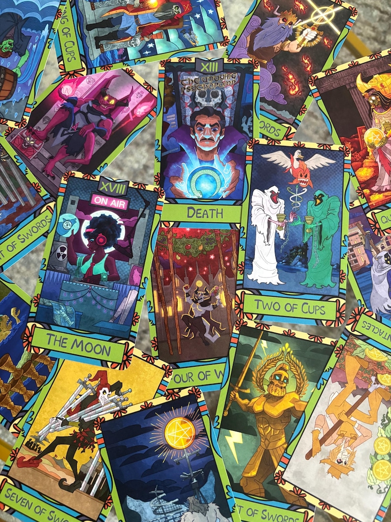 K&ouml;nnte beinhalten: Eine Sammlung farbenfroher Tarotkarten mit verschiedenen Illustrationen und Texten. Die Karten zeigen Bilder von Figuren, Symbolen und Texten wie "Death", "The Moon" und "Two of Cups". Die Karten haben einen gr&uuml;nen und floralen Rand.