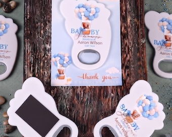 May include: Foot-shaped bottle openers with a white finish, featuring a graphic of blue and white balloons and the text Baby Shower, Aaron Wilson, and a date. The openers have a metal insert and a rectangular black magnet on the reverse side.