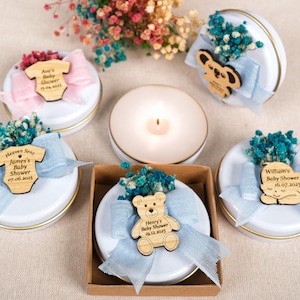 Puede incluir: Recuerdos de baby shower redondos y blancos, con bordes dorados, adornados con recortes de madera, lazos y flores secas. Cada recuerdo tiene un recorte de madera único, incluyendo un body, un koala, un oso y un bebé durmiendo. Personalizado.