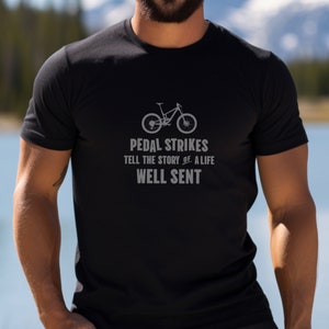 May include: A black t-shirt with a gray graphic of a mountain bike and the text "Pedal Strikes Tell the Story of a Life Well Sent".