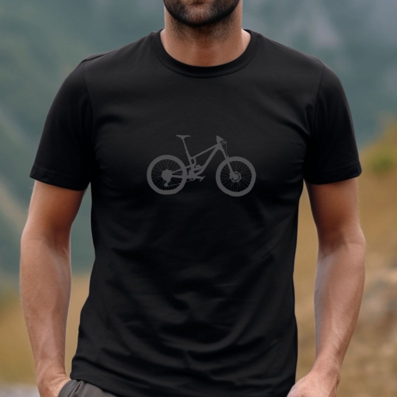 May include: Black t-shirt featuring a gray mountain bike graphic. The bicycle design is centered on the chest and includes details of the frame, wheels, and seat. The shirt is a crew neck style and appears to be made of a soft material.