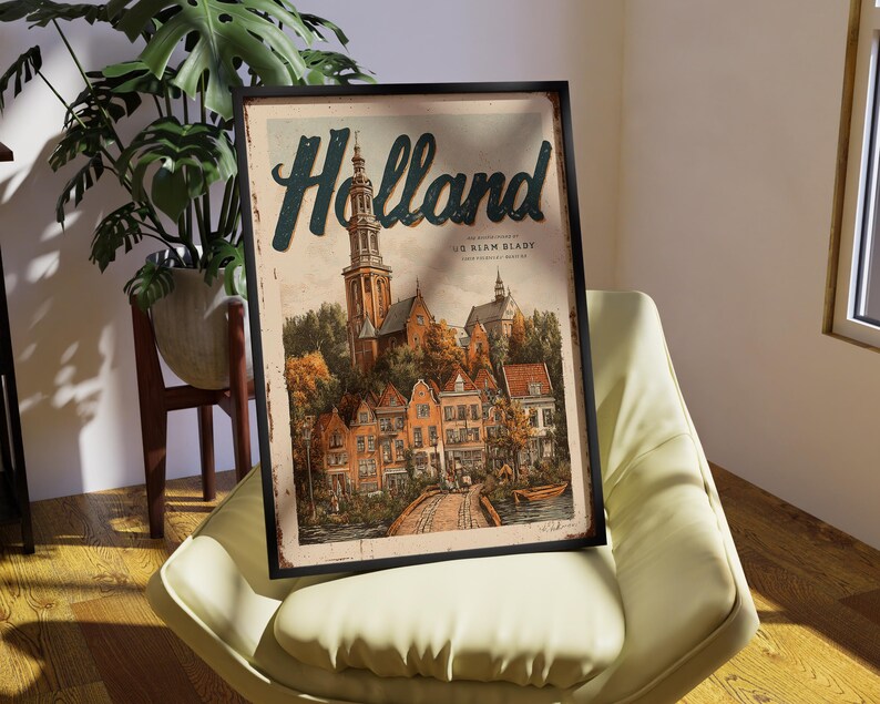 May include: A framed vintage-style poster with the word "Holland" in teal script. The artwork depicts a quaint European town with a church, bridge, and colorful buildings. The poster is in a black frame and rests on a cream-colored chair.