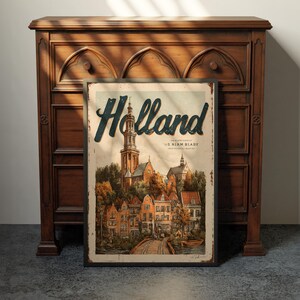 May include: A vintage-style Holland travel poster with a detailed illustration of a European town, featuring a church steeple and colorful buildings. The poster is framed and leans against a dark wooden cabinet.