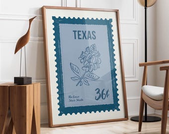 Könnte beinhalten: Gerahmter Druck mit einem blauen Briefmarken-Design, das das Wort "TEXAS" oben zeigt. Die Briefmarke zeigt eine Blumenillustration, den Text "The Lone Star State" und den Preis "36¢". Der Rahmen hat eine warme braune Farbe.