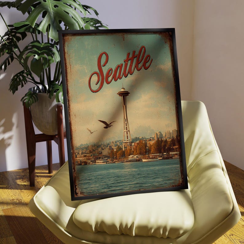 May include: A framed vintage-style print featuring the Seattle skyline, including the Space Needle and waterfront. The word "Seattle" is written in red script across the top. The print has a distressed, aged appearance, with a blue and tan color palette.