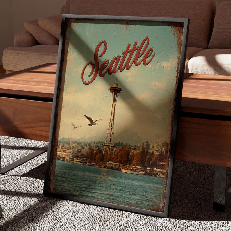 May include: A framed vintage-style print featuring the Seattle skyline, with the Space Needle prominently displayed. The word "Seattle" is written in red script across the top. The image has a distressed, aged appearance, with a blue and brown color palette.