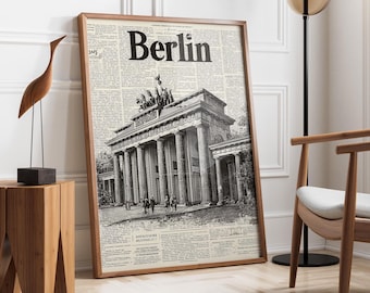 May include: A framed print featuring a black and white illustration of the Brandenburg Gate in Berlin. The word "Berlin" is printed in large, bold letters at the top. The background is a newspaper-style print.