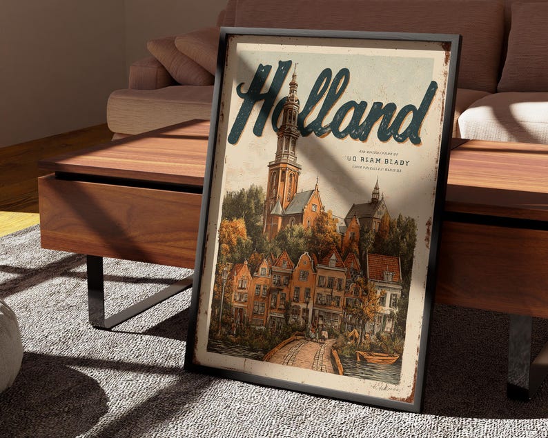 May include: Framed vintage-style poster with the word "Holland" in teal script. The artwork depicts a European town with a church, bridge, and colorful buildings. The poster is displayed on a wooden table.