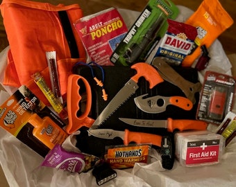 May include: A gift basket filled with hunting and outdoor gear. The basket includes a bright orange vest, a small saw, a knife, earplugs, hand warmers, a first aid kit, and other items.