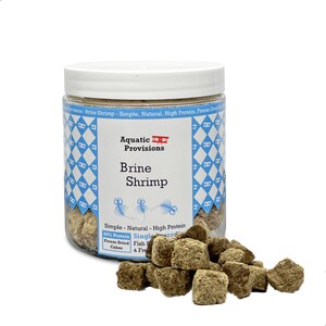 May include: A clear jar with a white lid filled with freeze-dried brine shrimp cubes. The jar has a blue and white label with the text "Aquatic Provisions Brine Shrimp" and "Simple - Natural - High Protein".