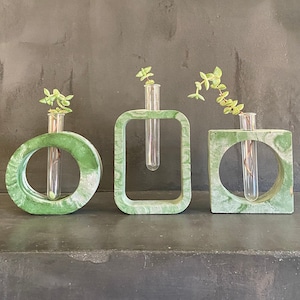 May include: Three green concrete vases with a circular, square, and rectangular shape. Each vase has a glass test tube inside for holding small plants or flowers.
