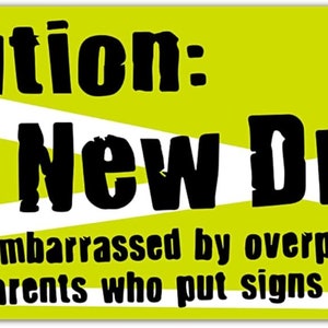 May include: A yellow and white sign with the text "Caution: New Driver" and a drawing of an orange traffic cone. The text below the main text reads "Embarrassed by overprotective parents who put signs on cars."