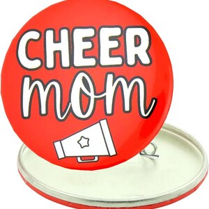 May include: Red round button with white text that says "CHEER MOM" and a white megaphone with a star on it.