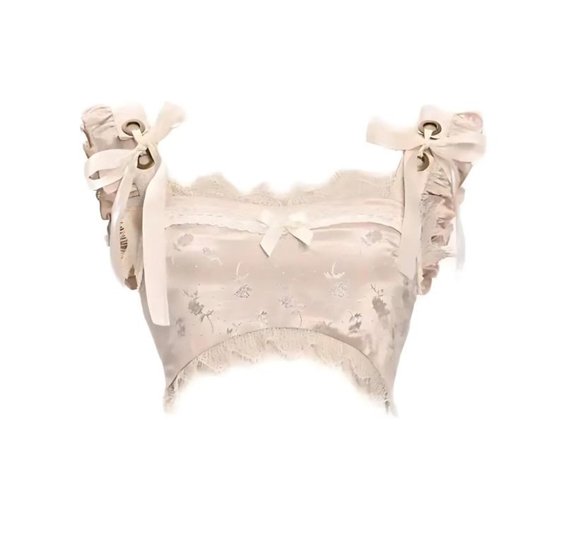 May include: A white satin crop top with lace trim and a floral pattern. The top has a square neckline and adjustable straps with bows and eyelets.