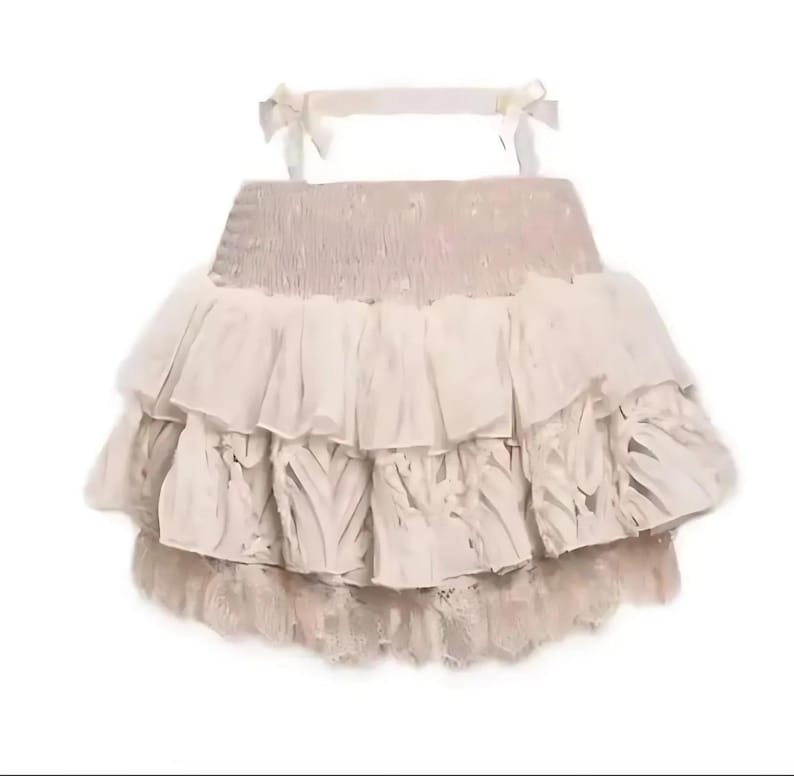 May include: A beige ruffled skirt with lace trim. The skirt has a gathered waistband and multiple layers of ruffles.