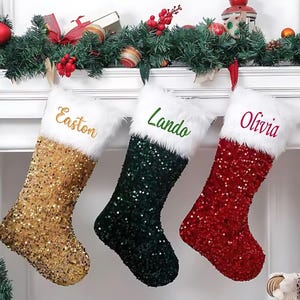 May include: Three Christmas stockings with faux fur trim and sequin fabric. The stockings are gold, green, and red. The stockings are personalized with the names Easton, Lando, and Olivia.