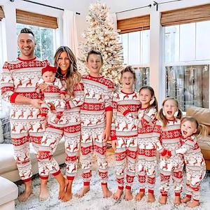 May include: A family of seven wearing matching red and white Christmas pajamas with a reindeer pattern. The pajamas have a snowflake design and are long-sleeved. The family is standing in front of a Christmas tree.