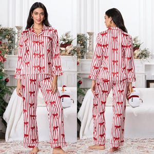 May include: A two-piece pajama set featuring a red and white striped pattern with red bow accents. The long-sleeved top has a button-down front and a collared neckline. The matching pants have a straight leg design. The pajamas are made of a soft, silky material.