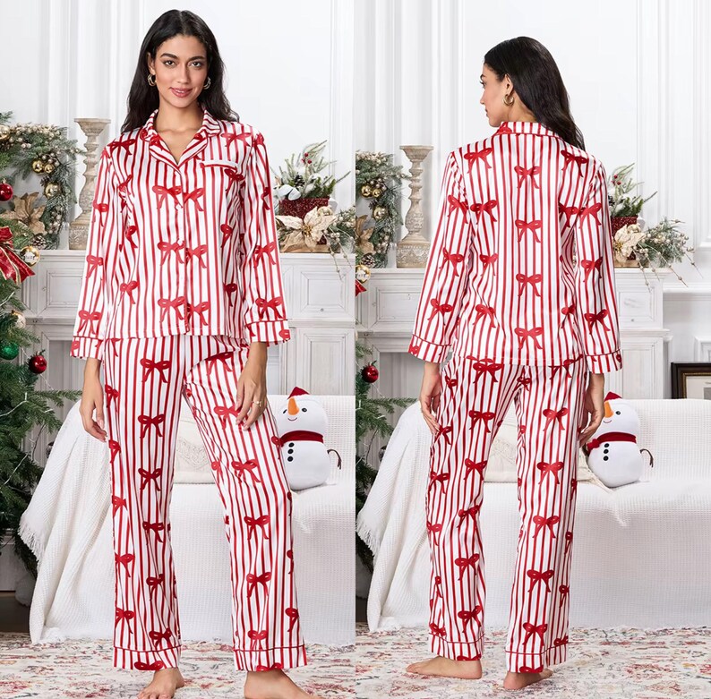 May include: A two-piece pajama set featuring a red and white striped pattern with red bow accents. The long-sleeved top has a button-down front and a collared neckline. The matching pants have a straight leg design. The pajamas are made of a soft, silky material.