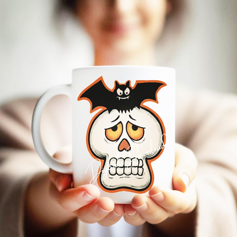 Może przedstawiać: Biały ceramiczny kubek z motywem Halloween. Projekt zawiera kresk&oacute;wkową czaszkę z pomarańczowymi akcentami i czarnego nietoperza. Kubek jest trzymany.