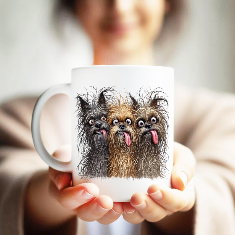 May include: A white ceramic mug featuring a graphic illustration of three shaggy dogs with wild fur, wide eyes, and tongues sticking out. The dogs are positioned side-by-side, with one black dog on the left, a tan dog in the center, and a brown dog on the right.