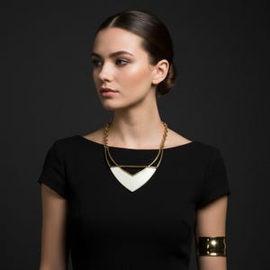 May include: A gold-toned necklace with a white geometric pendant is worn over a black dress. A matching gold cuff bracelet is on the arm. The jewelry has a modern, minimalist design.