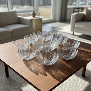 Pode incluir: Um conjunto de taças de vidro transparente com um design texturizado em forma de pétalas. A coleção inclui uma taça central grande rodeada por seis taças mais pequenas a condizer, todas com um rebordo recortado que imita uma flor.