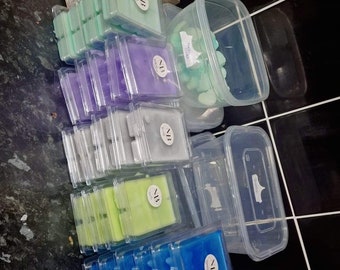 May include: Assortment of wax melts in various colors and scents, packaged in clear plastic containers. The wax melts are arranged in stacks and labeled with the initials "NB".