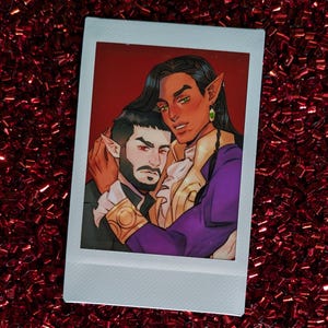 May include: Polaroid-style print with an illustration of two figures embracing. One has long black hair, pointed ears, and wears a purple jacket with gold accents. The other has a beard and wears a black suit. The background is red.