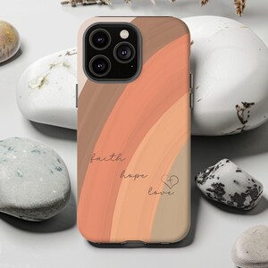 May include: A phone case featuring a design of warm-toned stripes in brown, peach, and beige. The words "faith, hope, love" are written in a delicate script, with a heart symbol. The case has a camera module.