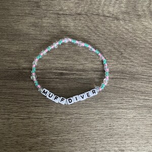May include: A pink and green beaded bracelet with the word "MUFFDIVER" spelled out in white letter beads.
