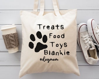 May include: A white canvas tote bag with black text that reads "Treats Food Toys Blankie #dogmom" and a black paw print.