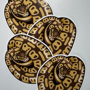 K&ouml;nnte beinhalten: Vier Aufkleber mit einer zusammengerollten Schlange mit einem braunen und beigen Muster. Die Schlange hat gr&uuml;ne Augen und einen wei&szlig;en Bauch. Die Aufkleber haben einen wei&szlig;en Rand und befinden sich auf wei&szlig;em Hintergrund.