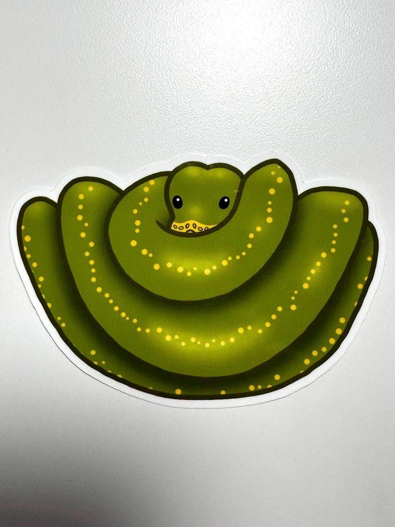 Pode incluir: Adesivo de uma cobra verde com manchas amarelas. A cobra est&aacute; enrolada e tem uma cara sorridente. O adesivo tem uma borda branca e est&aacute; em um fundo branco. Design divertido e l&uacute;dico.