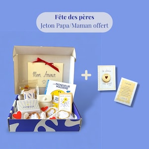 Peut inclure: Un coffret cadeau ouvert, contenant divers articles : un livre, des cartes et de petits accessoires. On peut voir un ruban rouge et une carte avec l'inscription "Mon Amour". Le tout est présenté sur un fond bleu.