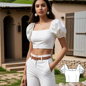 May include: A white crop top with puffed sleeves and a square neckline. The top is shown on a model wearing white pants and a brown belt.