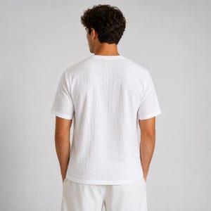 May include: A plain white short-sleeved t-shirt with a subtle vertical textured pattern. The garment features a classic crew neckline and a straight hemline, providing a clean and simple look. The fabric appears lightweight and breathable.