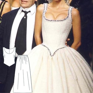 Puede incluir: Un vestido blanco sin mangas con ribete negro alrededor del escote y la cintura. El vestido tiene un corpiño ajustado y una falda completa.