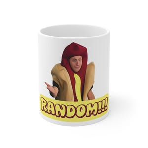 May include: White ceramic mug with a person in a hot dog costume. The costume includes a red bun hat and a mustard-colored outfit. The mug has the word "RANDOM!!!" in yellow and brown.