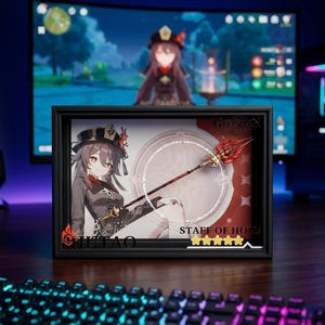 May include: A rectangular shadow box display featuring an illustration of the character Hu Tao and a miniature Staff of Homa. The display includes the text "HU TAO" and "STAFF OF HOMA" with five yellow stars, set against a red and white circular background.