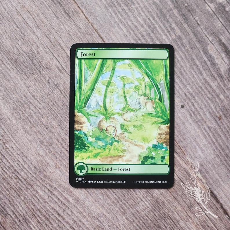 May include: A rectangular card with a green border and the word "Forest" at the top. The card features a watercolor painting of a forest scene with green foliage and a path. The text "Basic Land - Forest" is at the bottom.
