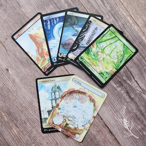 May include: A collection of Magic: The Gathering trading cards featuring various landscape illustrations. The cards include "Island," "Land," "Forest," "Command Tower," and "Sol Ring." The artwork showcases watercolor-style paintings of natural environments.
