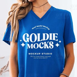 May include: A blue v-neck t-shirt with a white graphic design that says "GOLDIE MOCKS" and "MOCKUP STUDIO".