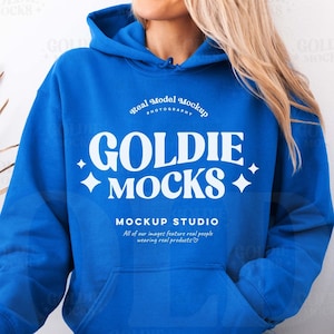 May include: A woman wearing a bright blue hoodie with the text "GOLDIE MOCKS" and "MOCKUP STUDIO" in white. The hoodie has a drawstring hood and a kangaroo pocket.