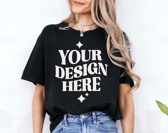 May include: A black t-shirt with the text "YOUR DESIGN HERE" in white lettering. The shirt is being worn by a person with long blonde hair and blue jeans.