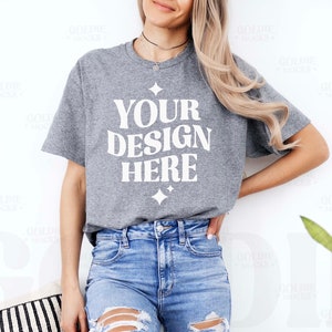 May include: A grey t-shirt with the text "YOUR DESIGN HERE" in white. The shirt is being worn by a person with long blonde hair and blue jeans.