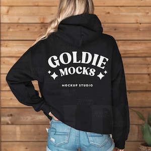 以下が含まれることがあります： 背面に「Goldie Mocks」と「Mockup Studio」と書かれた白いグラフィックが施された黒いパーカー